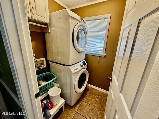 laundry area featuring stacked washing maching and dryer, tile patterned flooring, cabinet space, and baseboards