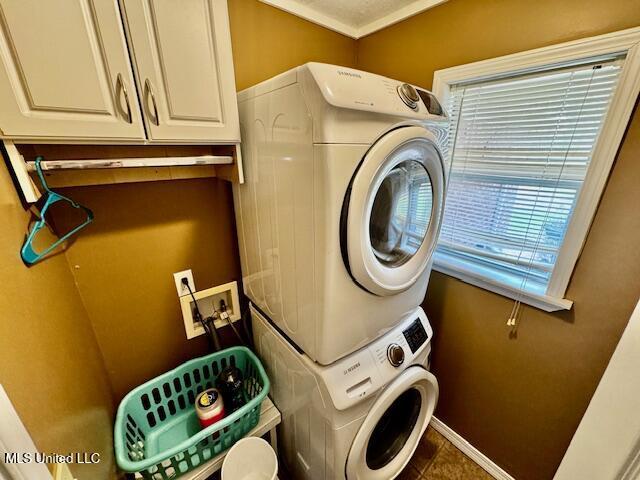 clothes washing area with laundry area, stacked washer / dryer, and baseboards