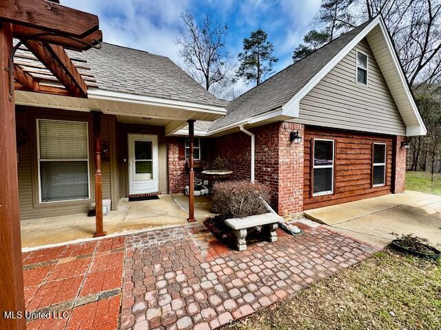 exterior space with a patio, brick siding, and roof with shingles