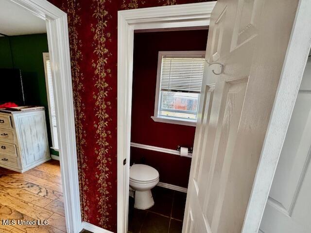 bathroom with toilet, wallpapered walls, baseboards, and tile patterned floors