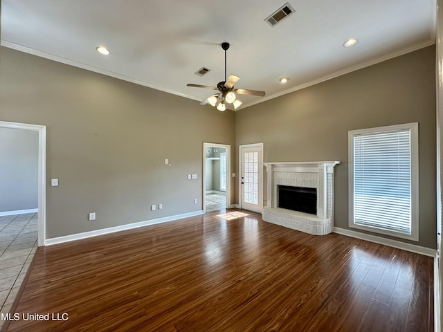 unfurnished living room with a brick fireplace, crown molding, ceiling fan, and dark wood-type flooring