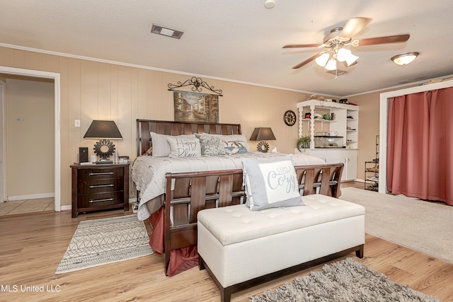 bedroom with ornamental molding, a textured ceiling, light wood-type flooring, and ceiling fan