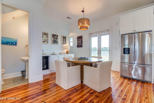 dining space with beverage cooler, ornamental molding, and light wood-style flooring