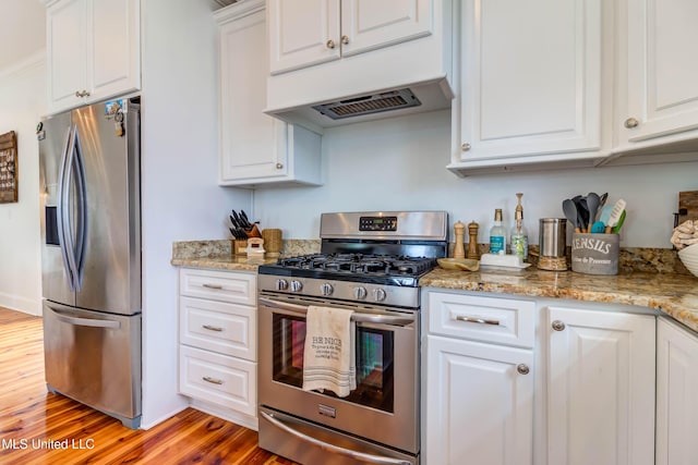 kitchen with light stone counters, appliances with stainless steel finishes, white cabinetry, and light wood-style floors