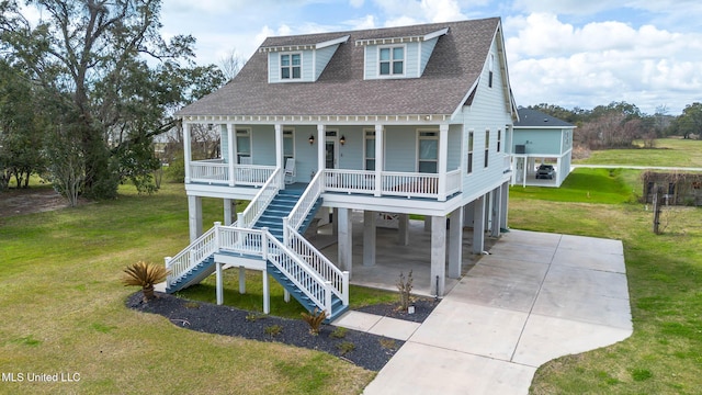 coastal home with covered porch, a shingled roof, stairs, and a front yard