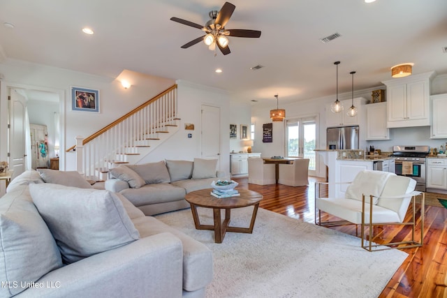 living room featuring visible vents, light wood-style flooring, stairway, ornamental molding, and recessed lighting