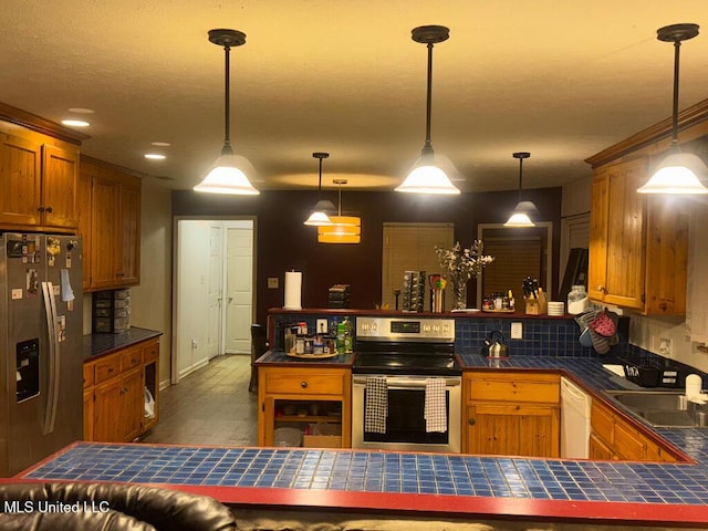 kitchen featuring brown cabinetry, a peninsula, wood finished floors, a sink, and appliances with stainless steel finishes