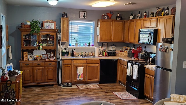 kitchen featuring a sink, visible vents, light countertops, black appliances, and dark wood finished floors