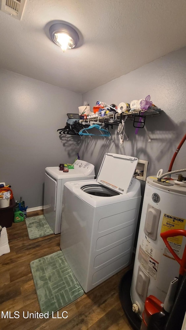 clothes washing area featuring washing machine and clothes dryer, water heater, visible vents, wood finished floors, and laundry area