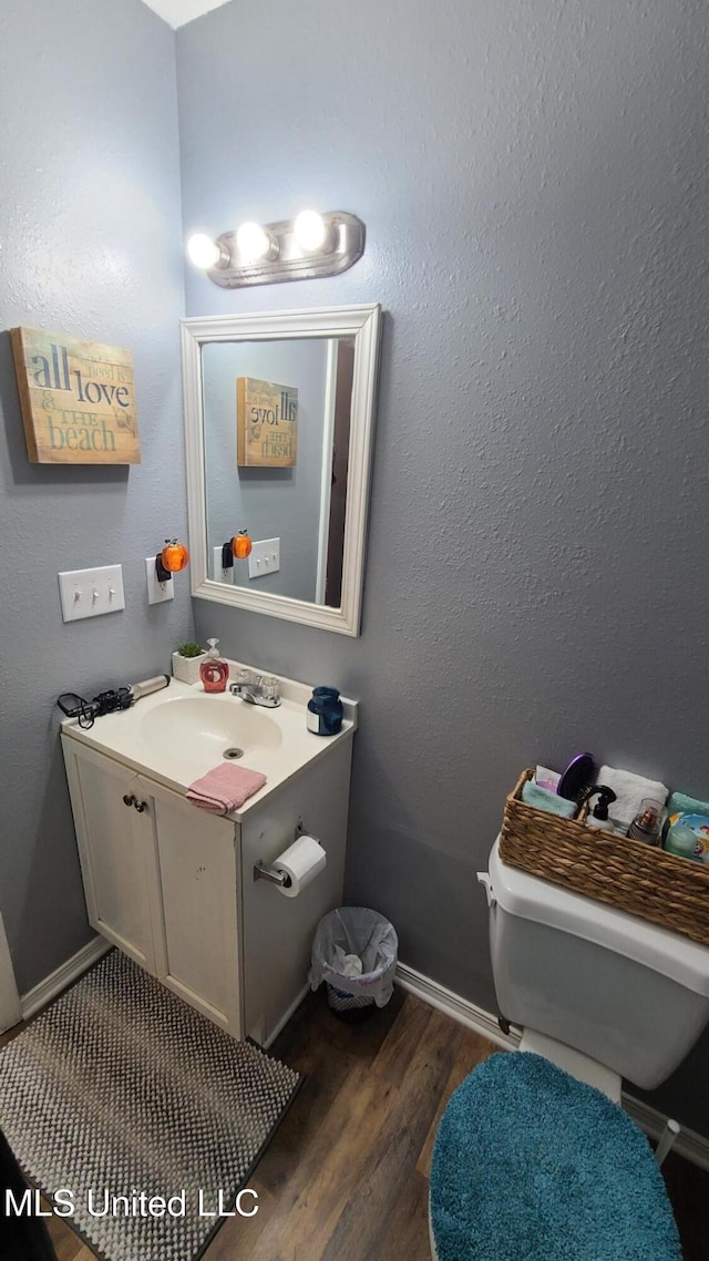 half bath featuring baseboards, vanity, toilet, and wood finished floors