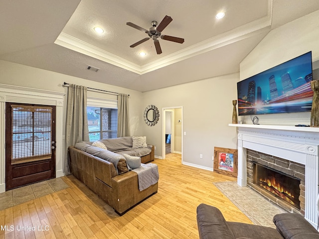 living room featuring a textured ceiling, ornamental molding, a raised ceiling, ceiling fan, and light hardwood / wood-style floors