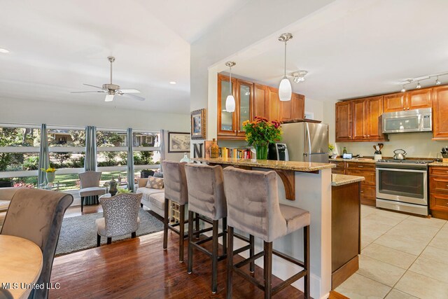 kitchen with a breakfast bar area, hanging light fixtures, stainless steel appliances, light stone countertops, and ceiling fan