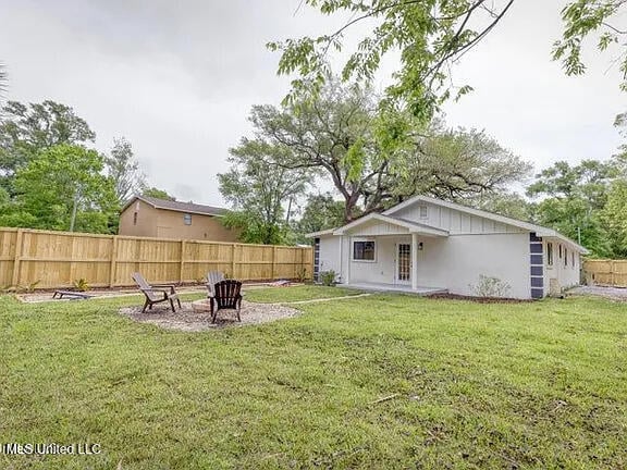 rear view of property with a fenced backyard, a lawn, and a fire pit