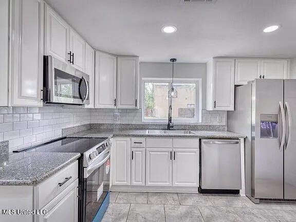 kitchen featuring appliances with stainless steel finishes, white cabinets, decorative backsplash, and light stone counters