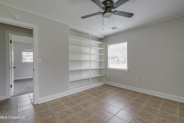 tiled empty room featuring crown molding, built in shelves, and ceiling fan