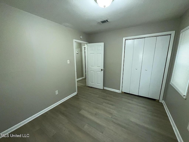 unfurnished bedroom with dark wood-style flooring, a closet, visible vents, and baseboards