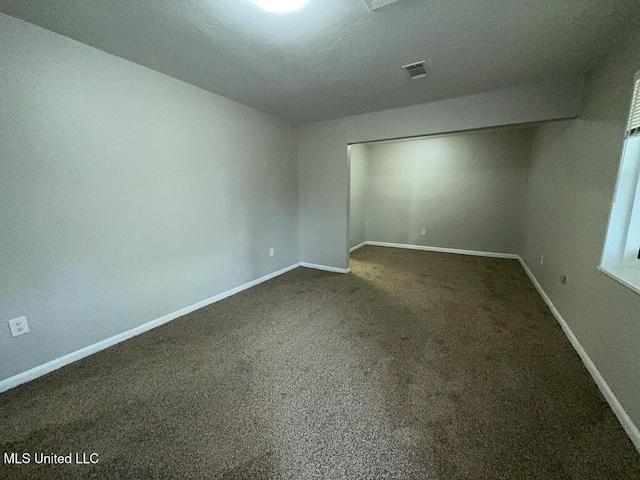 unfurnished room with dark colored carpet, visible vents, and baseboards