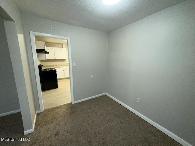 spare room with a textured ceiling, dark colored carpet, and baseboards