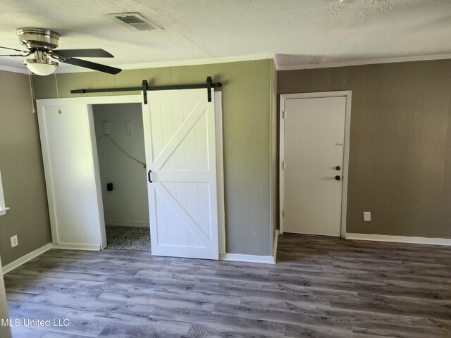 unfurnished bedroom featuring crown molding, a barn door, wood-type flooring, and ceiling fan