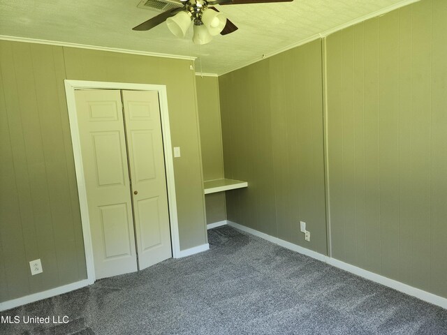 unfurnished bedroom with a closet, ornamental molding, dark carpet, and ceiling fan