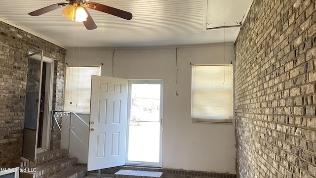 foyer entrance with ceiling fan and brick wall