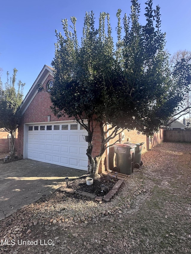 view of side of property featuring brick siding, concrete driveway, and fence