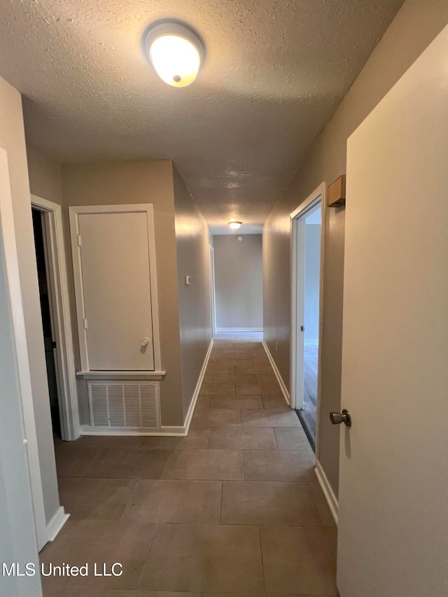 hall featuring dark tile patterned floors and a textured ceiling