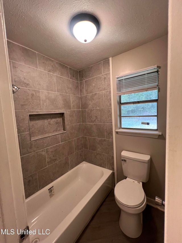 bathroom with a textured ceiling, toilet, and tiled shower / bath