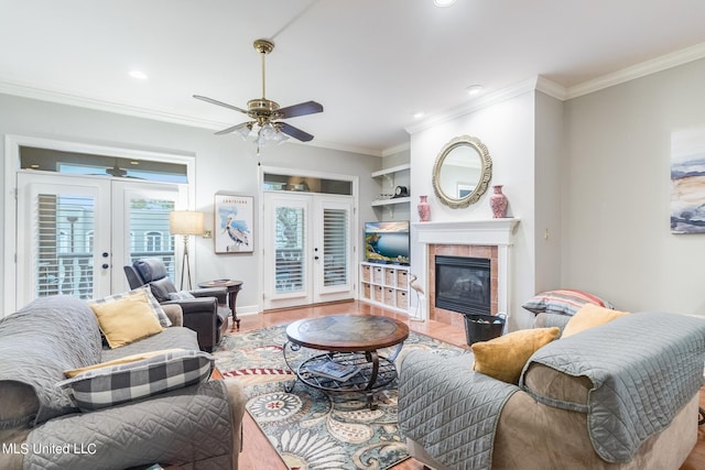 living room featuring french doors, a tiled fireplace, wood-type flooring, and ornamental molding