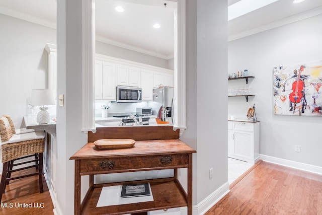 kitchen with sink, stainless steel appliances, white cabinets, ornamental molding, and light hardwood / wood-style flooring