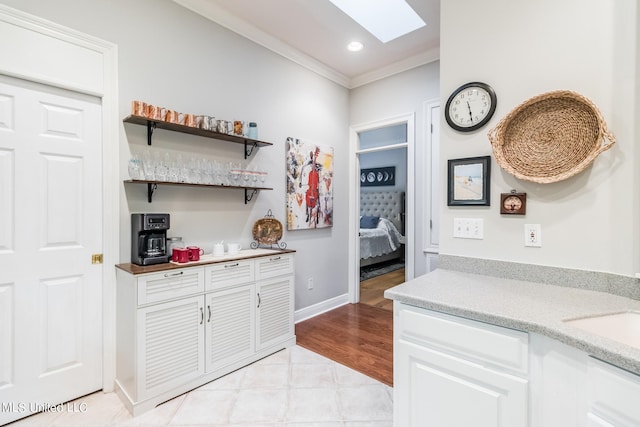 bar with a skylight, sink, white cabinetry, ornamental molding, and light hardwood / wood-style flooring