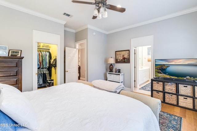 bedroom with ceiling fan, a spacious closet, wood-type flooring, crown molding, and ensuite bath