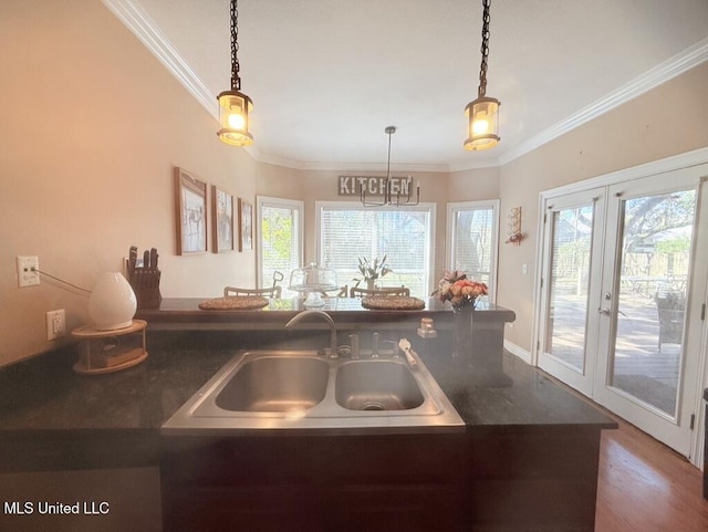 kitchen with crown molding, dark countertops, decorative light fixtures, and a sink