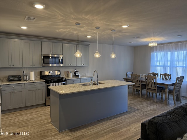 kitchen featuring appliances with stainless steel finishes, sink, decorative light fixtures, light hardwood / wood-style floors, and an island with sink