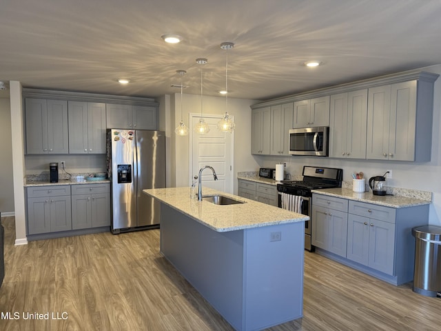 kitchen featuring light stone countertops, appliances with stainless steel finishes, sink, light hardwood / wood-style floors, and hanging light fixtures