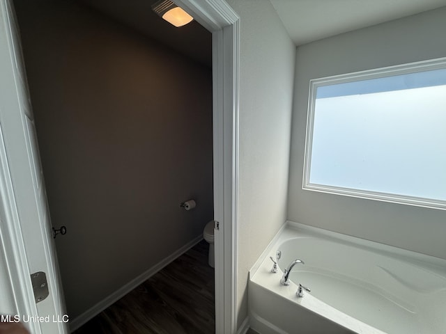 bathroom with a bathing tub, hardwood / wood-style floors, and toilet