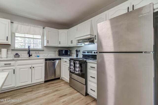 kitchen with white cabinets, appliances with stainless steel finishes, custom exhaust hood, sink, and light wood-type flooring