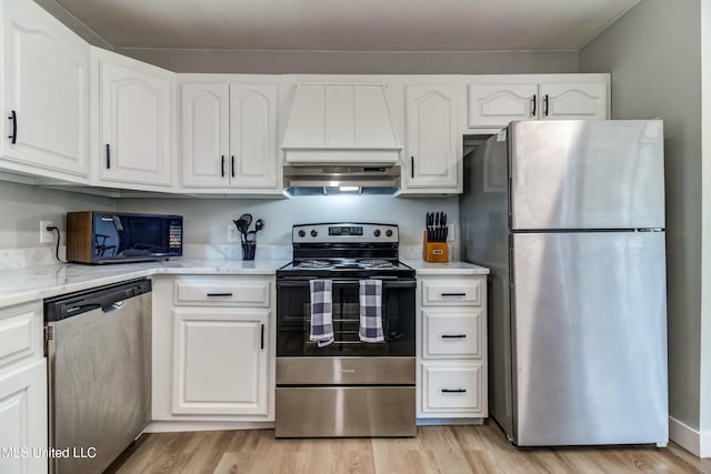 kitchen with white cabinetry, stainless steel appliances, light wood-type flooring, range hood, and light stone counters