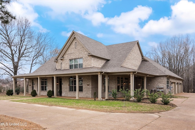 view of front of house featuring brick siding, roof with shingles, concrete driveway, covered porch, and a front lawn