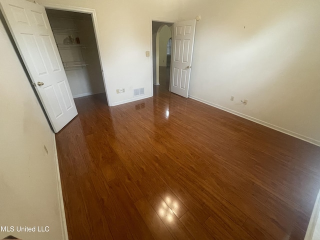 unfurnished bedroom featuring visible vents, arched walkways, baseboards, and dark wood-style floors
