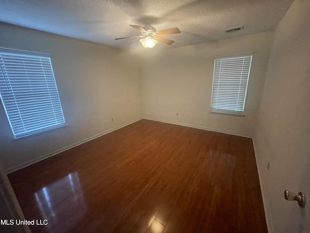 spare room with a textured ceiling, a ceiling fan, wood finished floors, and visible vents