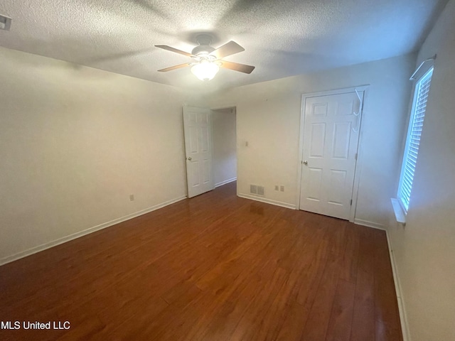 unfurnished bedroom featuring a textured ceiling, dark wood finished floors, a ceiling fan, baseboards, and visible vents