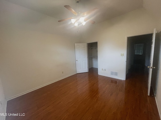 unfurnished bedroom featuring a walk in closet, baseboards, dark wood-type flooring, visible vents, and a closet