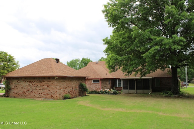 rear view of property featuring roof with shingles, a yard, a sunroom, and brick siding