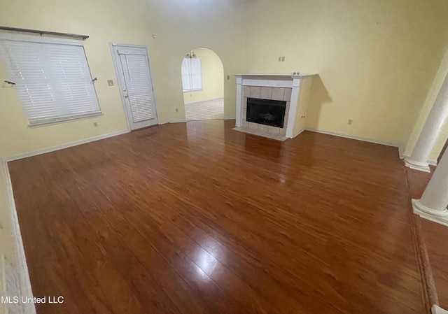 unfurnished living room featuring decorative columns, arched walkways, a fireplace, wood finished floors, and baseboards