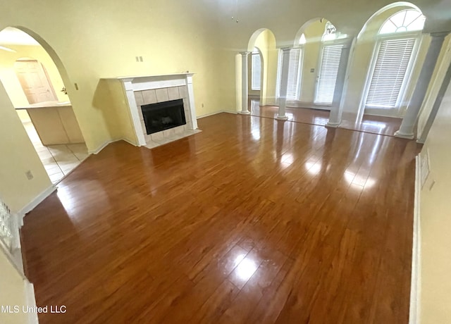 unfurnished living room with arched walkways, decorative columns, wood finished floors, and a tile fireplace