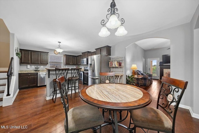 dining area featuring arched walkways, dark wood-style flooring, baseboards, and a chandelier