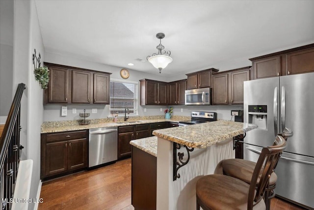kitchen featuring stainless steel appliances, a sink, dark brown cabinets, a breakfast bar area, and hanging light fixtures