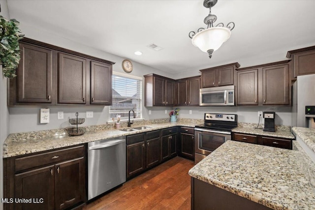 kitchen featuring stainless steel appliances, a sink, dark brown cabinetry, dark wood-style floors, and hanging light fixtures