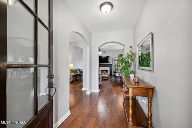foyer featuring arched walkways, a fireplace, hardwood / wood-style floors, ceiling fan, and baseboards